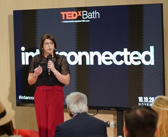 Claire, a Trans Woman in red trousers and black blouse, speaking at a TEDx event